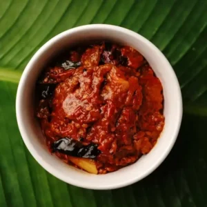 A cup full of DNachiys Tomato Pickle on a banana leaf