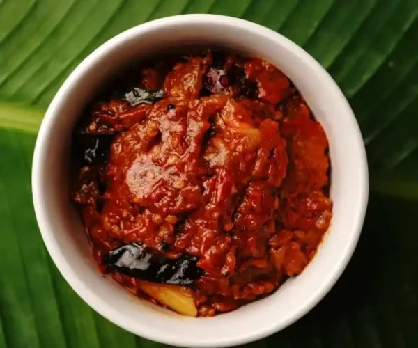A cup full of DNachiys Tomato Pickle on a banana leaf A cup full of DNachiys Tomato Pickle on a banana leaf