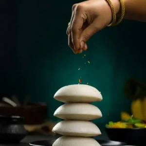 A hand sprinkling DNachiys Veg Idli Podi/Chutney Powder over the hot Idlis